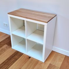 a white shelf with wooden top sitting on the floor next to a wall and hardwood floors