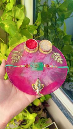 a hand holding a pink glass plate with two small cupcakes on top of it