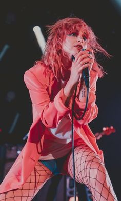 a woman with red hair and fishnet stockings on holding a microphone in her hand