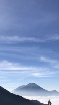 there is a mountain in the distance with clouds on it and blue sky above them