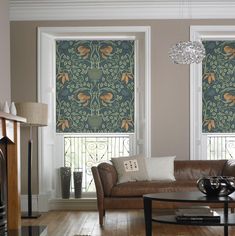 a living room with two windows covered in roman shades and brown leather couches next to a coffee table