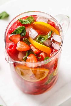 a pitcher filled with fruit and ice sitting on top of a white table next to sliced lemons