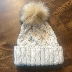 a white beanie with a pom - pom on top sitting on a wooden table