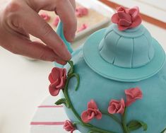 a person is decorating a blue cake with pink flowers on it and holding a plastic spoon