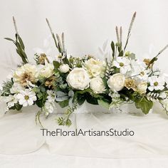 white flowers and greenery are arranged in an arrangement