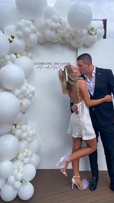 a man and woman standing next to each other in front of a wall with white balloons