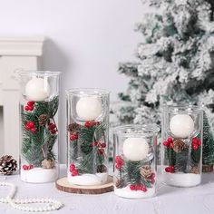 three glass vases filled with white candles on top of a table next to a christmas tree