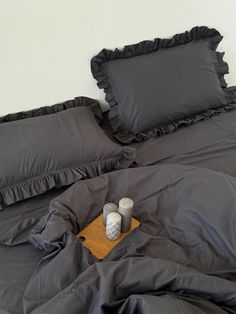 a bed with black ruffled sheets and two vases on the bottom of it