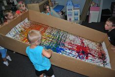 children are playing with an art project in a cardboard box that is filled with paint