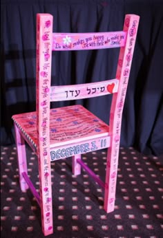 a pink wooden chair with hebrew writing on the back and sides, decorated with flowers