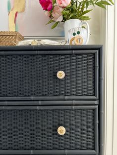 a black wicker dresser with flowers on top and a white vase in the background