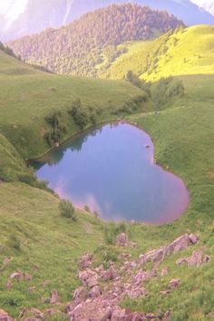 there is a small lake in the middle of this mountain side area that has grass and rocks around it