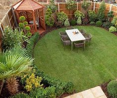 a small backyard with a table and chairs in the center, surrounded by greenery