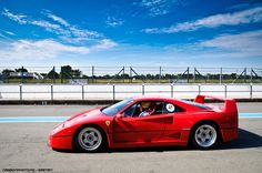 a red sports car driving down a race track in front of a blue sky with white clouds