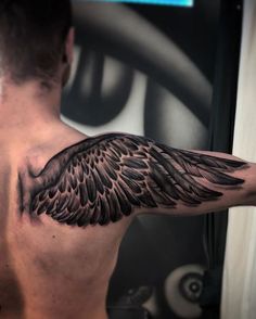 a man's back with an angel wing tattoo on his upper arm and shoulder