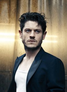 a man standing in front of a metal wall wearing a black jacket and white shirt