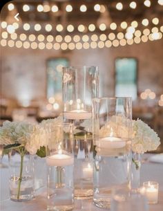 the centerpieces are filled with white flowers, candles and votive glass vases