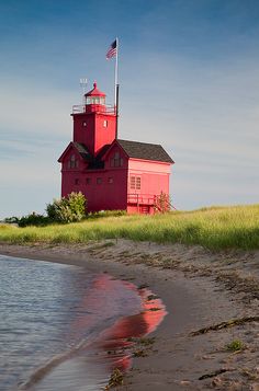 a red light house sitting on top of a lush green field next to the ocean