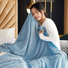 a woman wrapped up in a blue and white checkered blanket on top of a bed