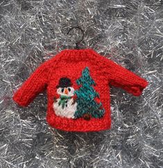 a knitted christmas sweater ornament with a snowman and tree on it