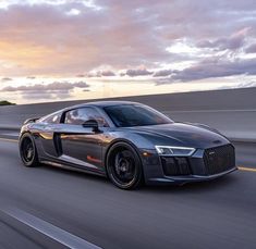 an audi sports car driving down the road at sunset or dawn with clouds in the background