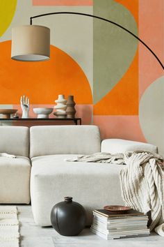 a modern living room with an orange and yellow wall mural behind the couch, coffee table, vases and books on the floor