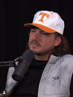 a man with long hair wearing a hat and holding a microphone in front of him