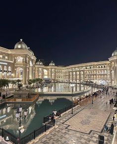 people are walking around in front of a large building with lights on it at night