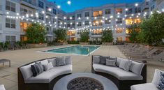 an outdoor seating area with lights strung over the swimming pool and lounge chairs around it