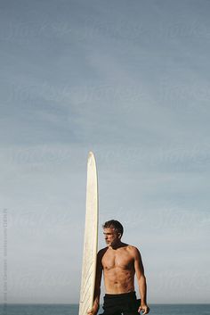 a shirtless man holding a surfboard on the beach