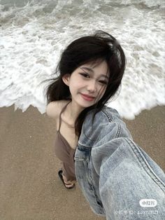 a young woman standing on top of a sandy beach next to the ocean with her feet in the sand