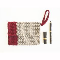 a crocheted purse with a red and white stripe next to a pen on a white surface