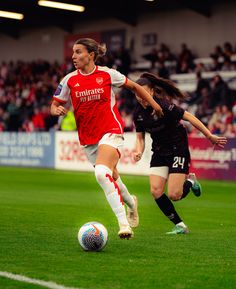 two women playing soccer on a field with fans in the stands watching from the stands