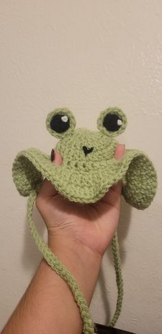 a hand holding up a green crocheted frog hat with eyes and nose,