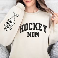 a woman wearing a hockey mom sweatshirt holding up her mitt and looking at the camera