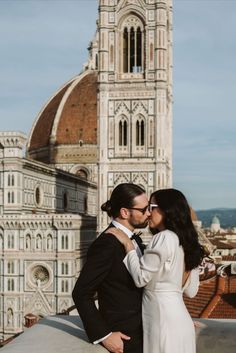 a man and woman standing next to each other in front of a building with a clock tower