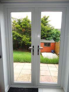 two double doors open in front of a backyard area with grass and trees behind them