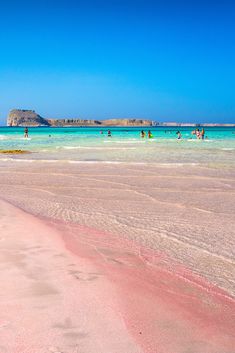 people are swimming in the blue water and pink sand