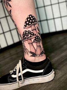 a woman's leg with black and white tattoos on it, including an image of mushrooms