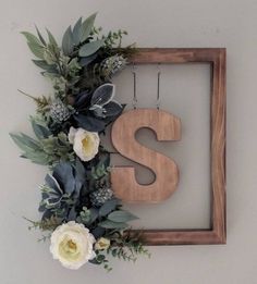 the letter s is surrounded by flowers and greenery in front of a wooden frame