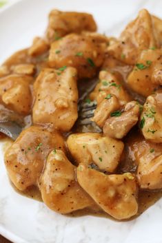 a white plate topped with chicken covered in gravy and a fork next to it