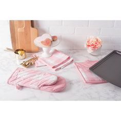 pink kitchen accessories laid out on a white counter top with flowers and cake in the background