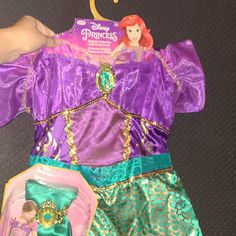 the little mermaid dress is being held up by someone's hand and has a doll in it