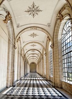 an empty hallway with large windows and checkered flooring on one side, in the middle of a building