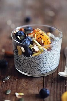 a glass bowl filled with blueberries, oranges and nuts on top of a wooden table