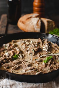 a skillet filled with meat and mushrooms in gravy next to some bread