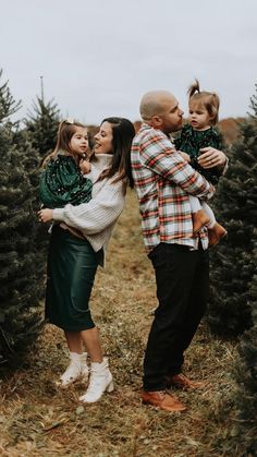 a man and woman holding two children in their arms while standing next to a christmas tree