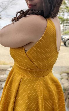 a woman in a yellow polka dot dress poses for the camera with her arms crossed