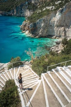 a woman is standing on some steps near the water and cliffs with blue water in the background