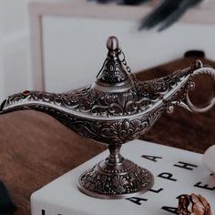 an ornate silver teapot sitting on top of a white box next to a pine cone